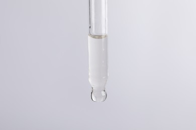 Photo of Dripping cosmetic serum from pipette on light grey background