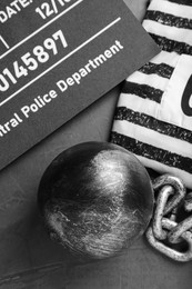 Photo of Metal ball with chain, prison uniform and mugshot letter board on grey table, flat lay
