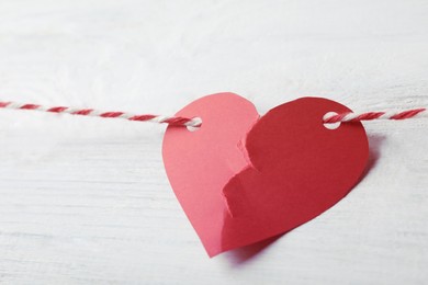 Image of Broken red paper heart and rope on white wooden table, closeup. Cheating concept