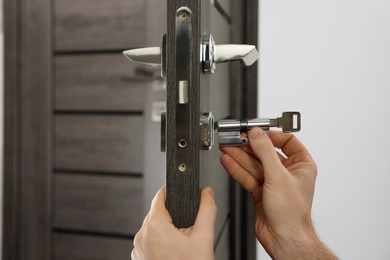 Photo of Handyman changing core of door lock indoors, closeup