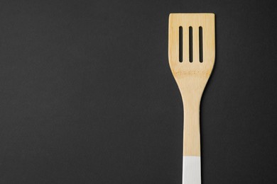 Photo of One wooden spatula on black background, top view. Space for text