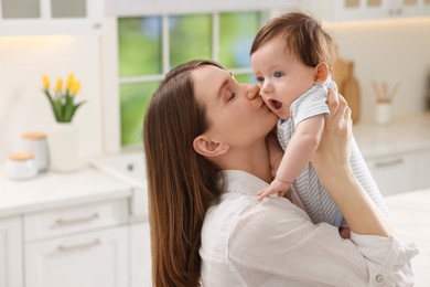 Photo of Happy mother kissing her little baby in kitchen