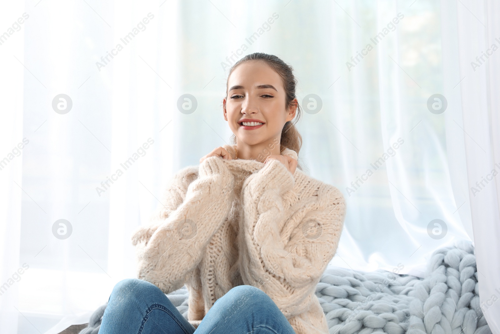 Photo of Beautiful teenage girl in warm cozy sweater sitting near window at home