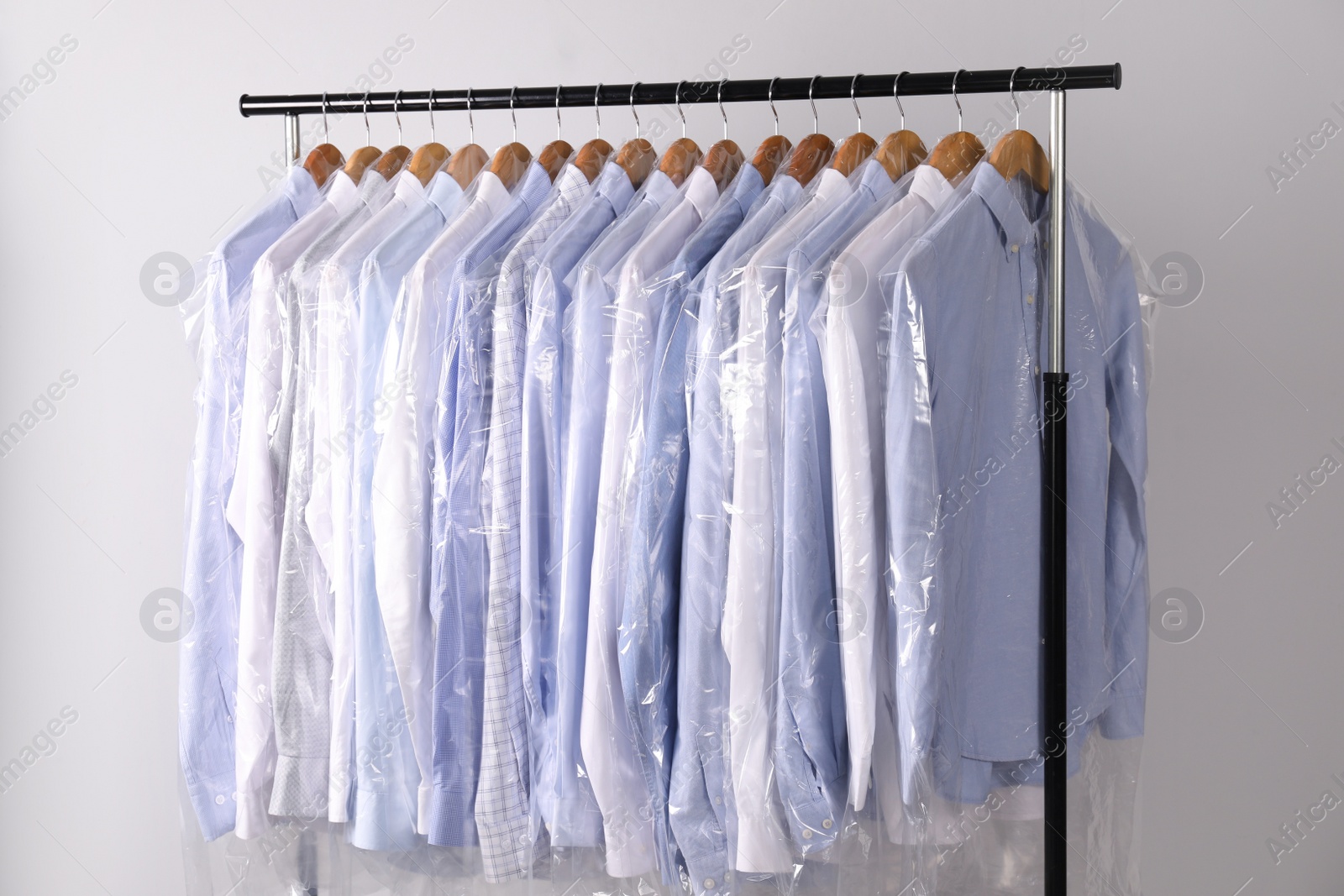 Photo of Hangers with shirts in dry cleaning plastic bags on rack against light background