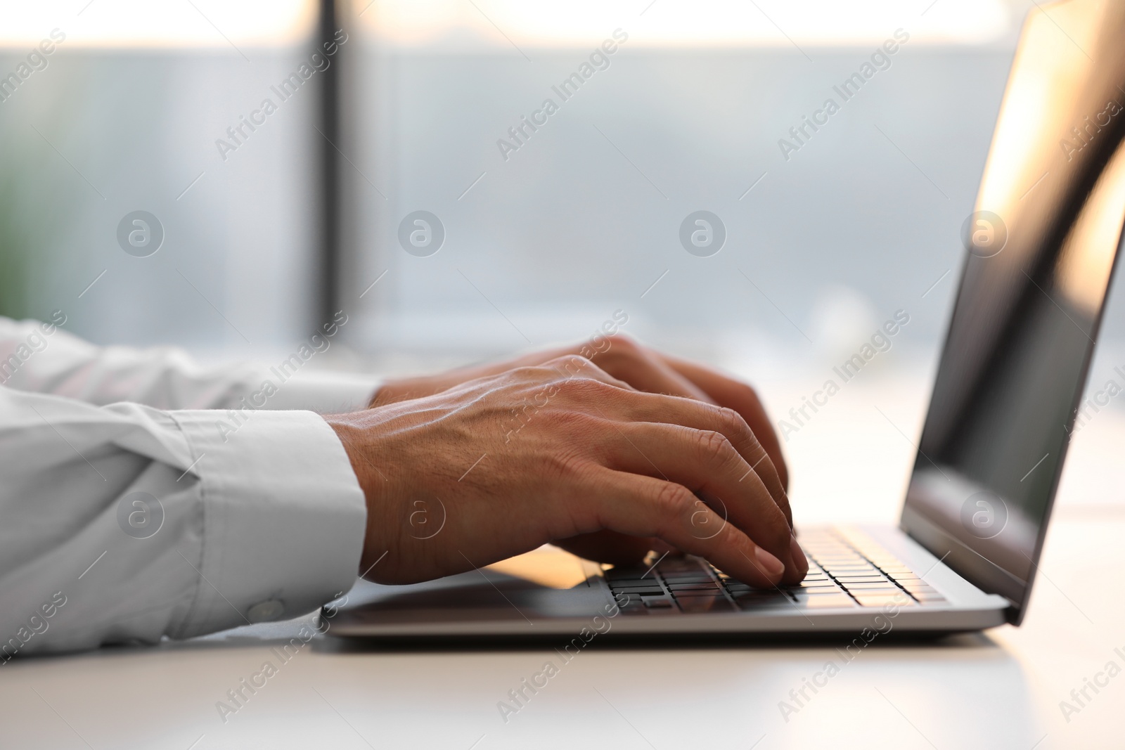 Photo of Man using modern laptop at white desk in office, closeup