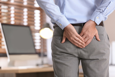 Photo of Man suffering from hemorrhoid in office, closeup