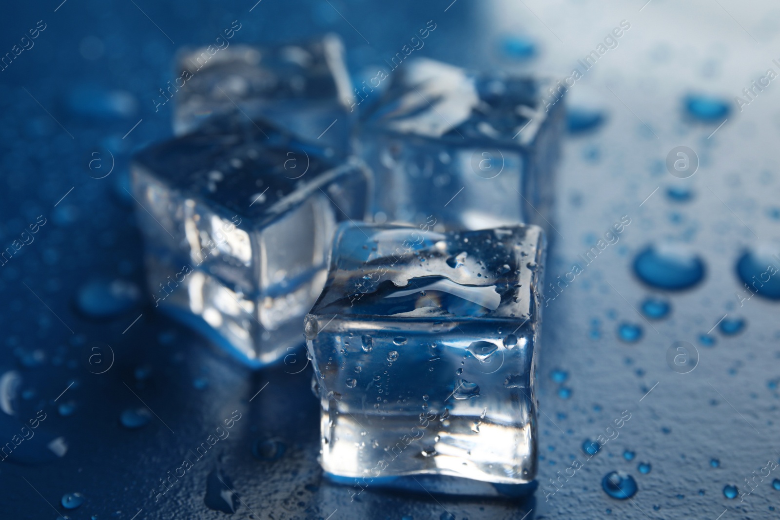 Photo of Ice cubes with water drops on blue background, closeup