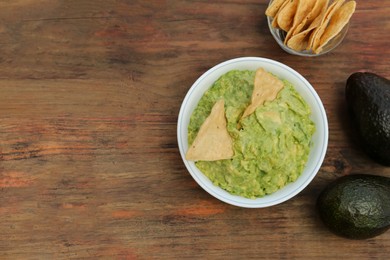 Photo of Delicious guacamole, avocados and nachos on wooden table, flat lay. Space for text