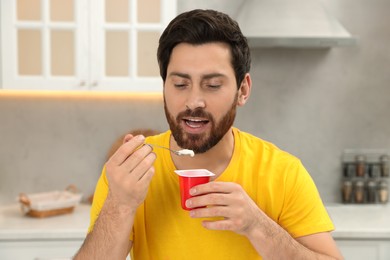 Photo of Handsome man eating delicious yogurt in kitchen