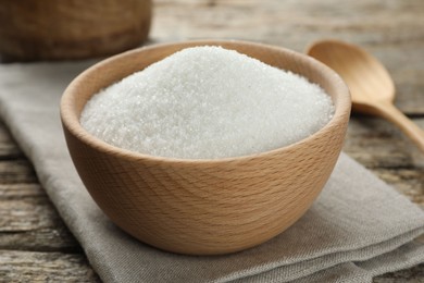 Photo of Granulated sugar in bowl on wooden table, closeup