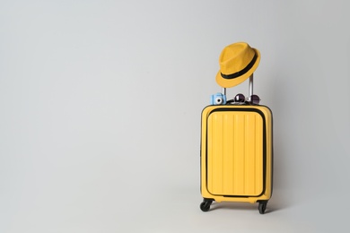 Photo of Travel suitcase with hat, camera and sunglasses on light grey background, space for text. Summer vacation