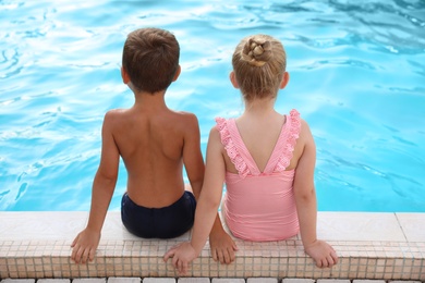 Cute little children sitting at outdoor swimming pool