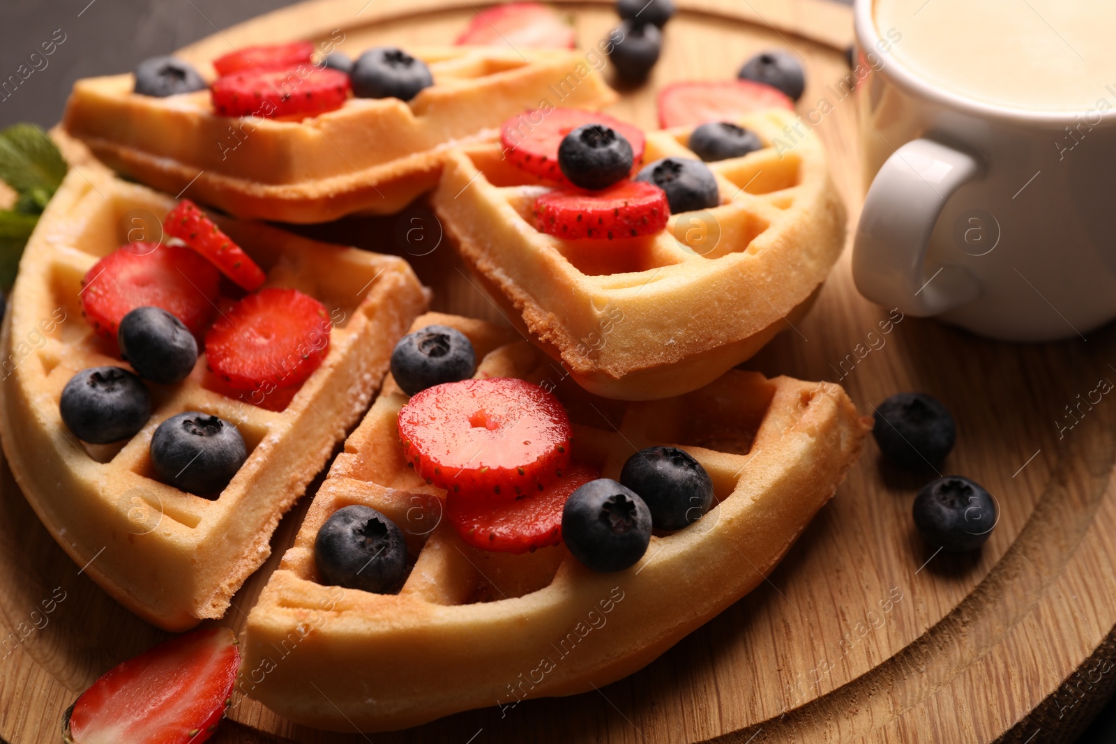 Photo of Tasty Belgian waffles with fresh berries on wooden board, closeup