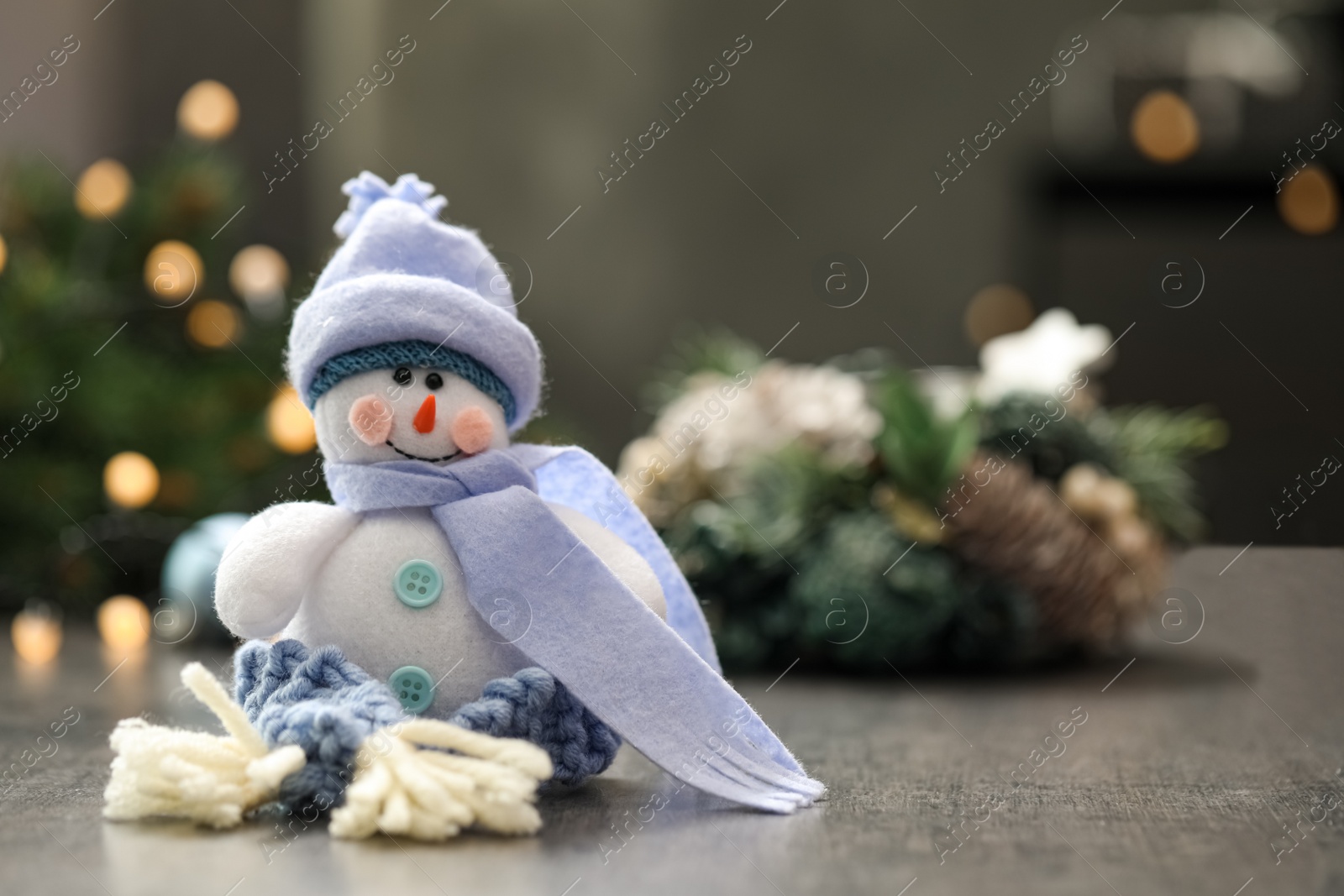 Photo of Snowman toy on grey table against blurred festive lights, space for text. Christmas decoration