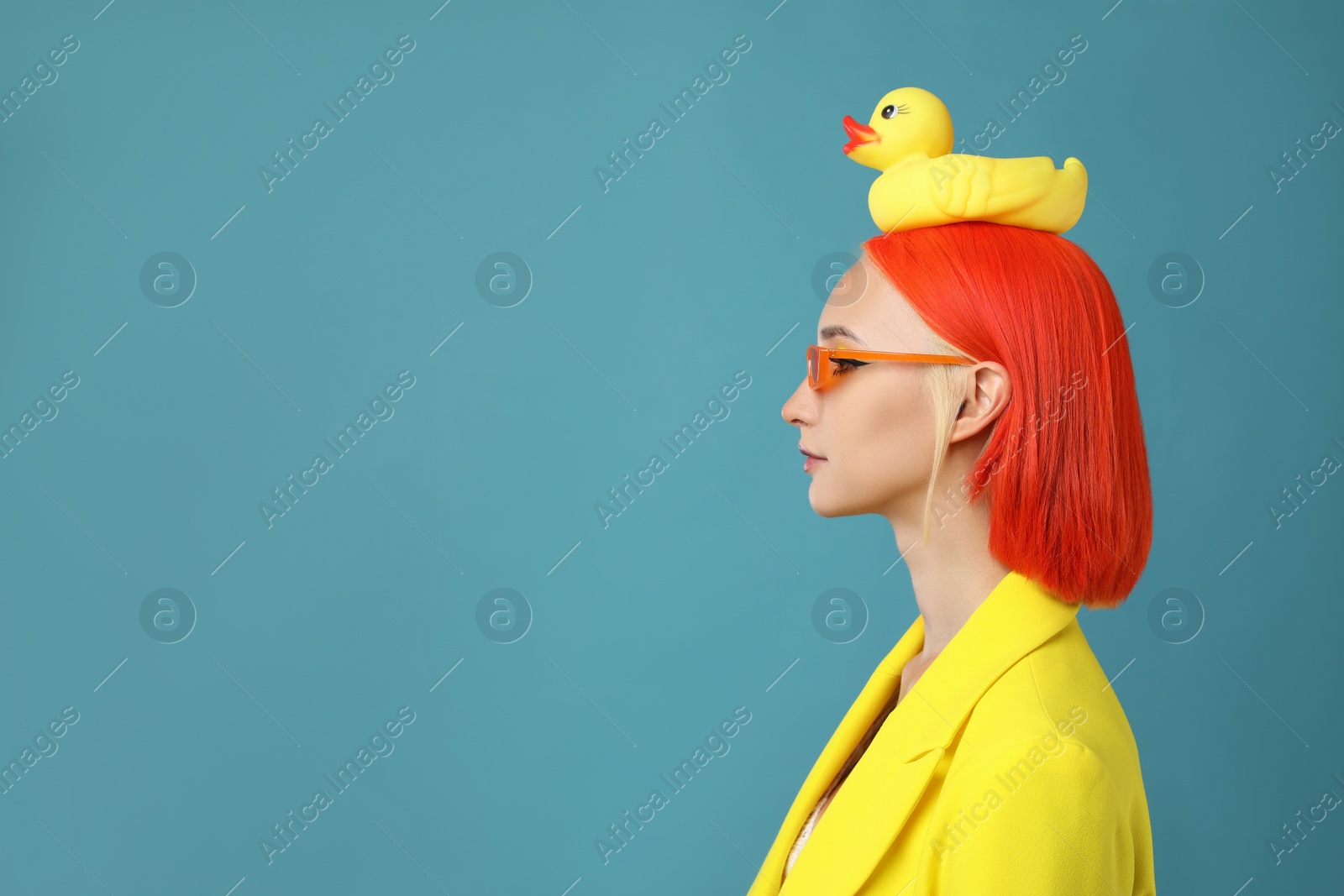 Photo of Beautiful young woman with bright dyed hair and toy duck on turquoise background, space for text