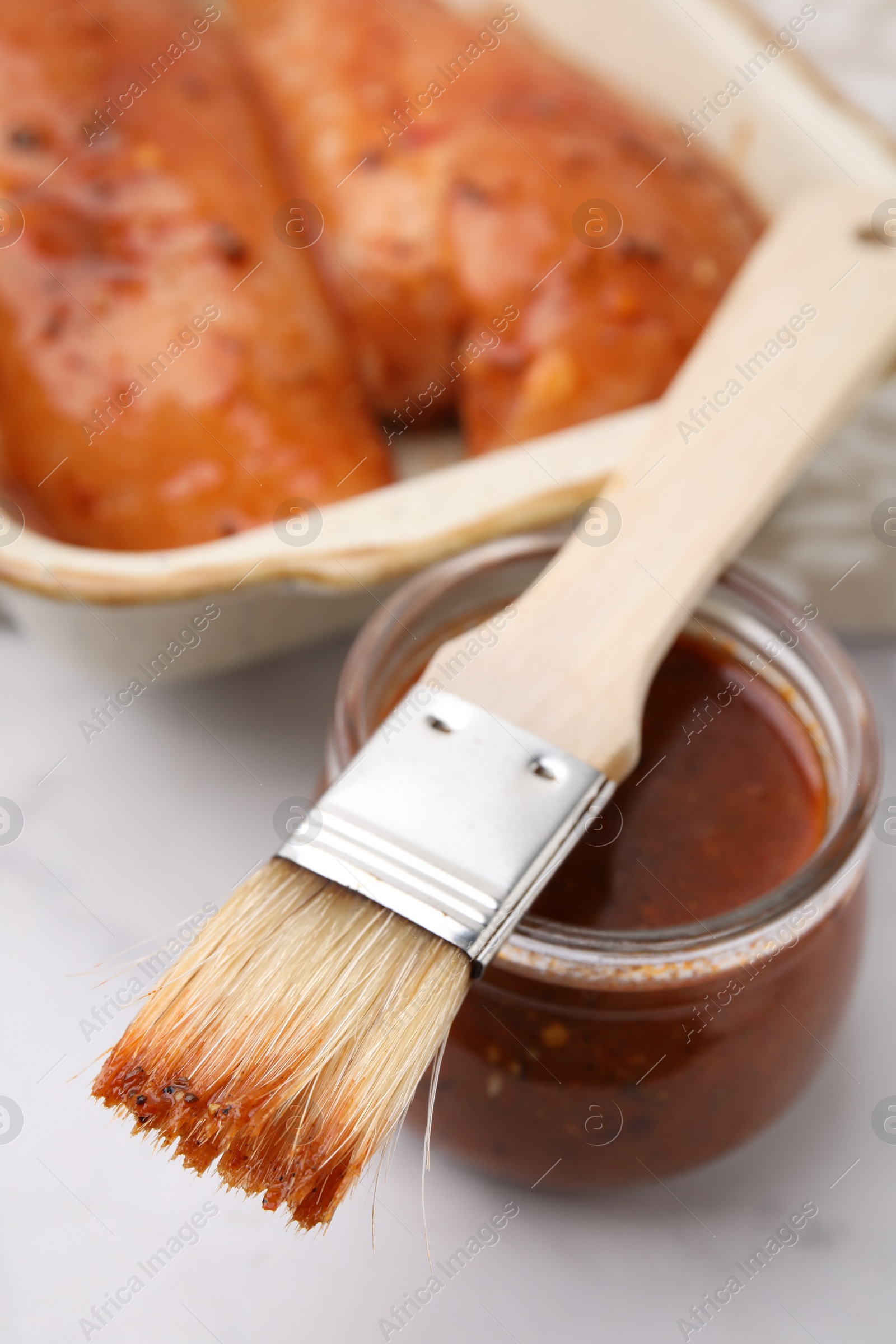 Photo of Fresh marinade, basting brush and raw chicken fillets on white table, closeup