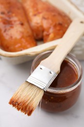 Photo of Fresh marinade, basting brush and raw chicken fillets on white table, closeup