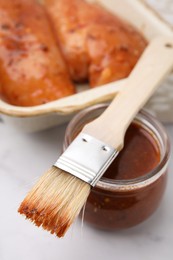 Fresh marinade, basting brush and raw chicken fillets on white table, closeup