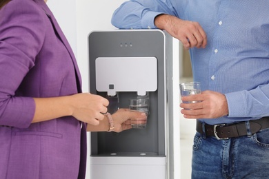 Photo of Employees taking glasses of water from cooler in office, closeup