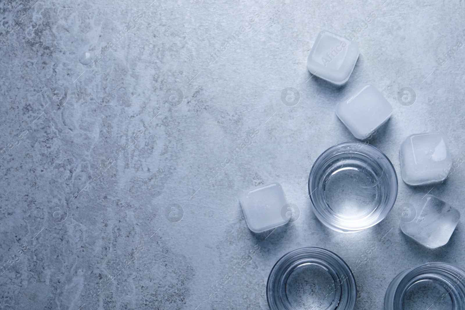 Photo of Shot glasses of vodka with ice on light grey table, flat lay. Space for text