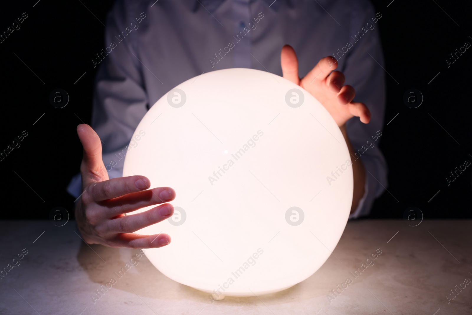 Photo of Businesswoman using glowing crystal ball to predict future at table in darkness, closeup. Fortune telling