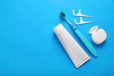 Photo of Container with dental floss, toothpaste and toothbrush on light blue background, flat lay. Space for text
