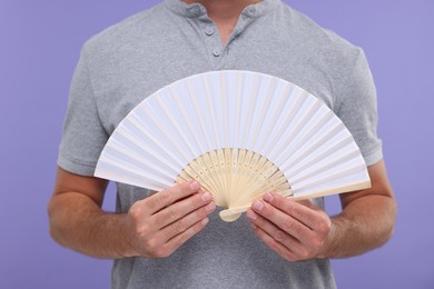 Photo of Man holding hand fan on purple background, closeup