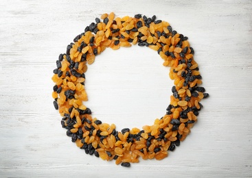 Photo of Round frame made of raisins on wooden background, space for text. Dried fruit as healthy snack