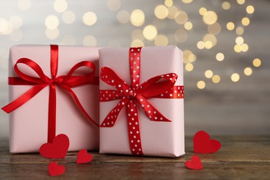 Beautiful gift boxes with decorative red hearts on wooden table against blurred lights