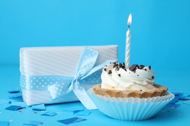 Photo of Birthday cupcake with candle and gift box on light blue background