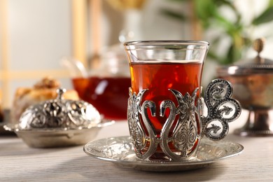 Photo of Glass of traditional Turkish tea in vintage holder on white wooden table, closeup. Space for text