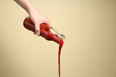 Woman pouring tasty ketchup from bottle on beige background, closeup. Space for text