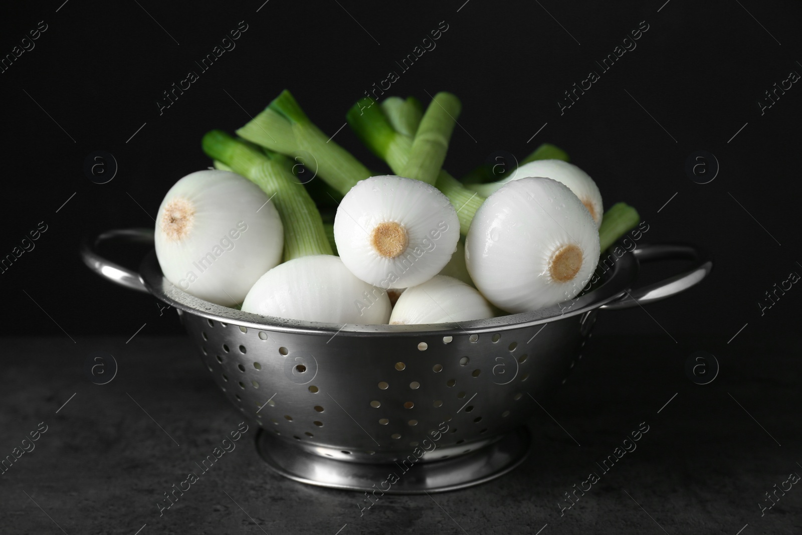 Photo of Colander with green spring onions on black table, closeup