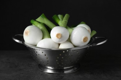 Photo of Colander with green spring onions on black table, closeup