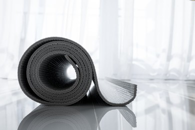 Photo of Rolled karemat or fitness mat on floor indoors, closeup. Space for text