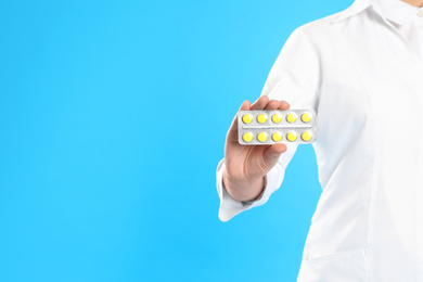 Professional pharmacist with pills on light blue background, closeup. Space for text