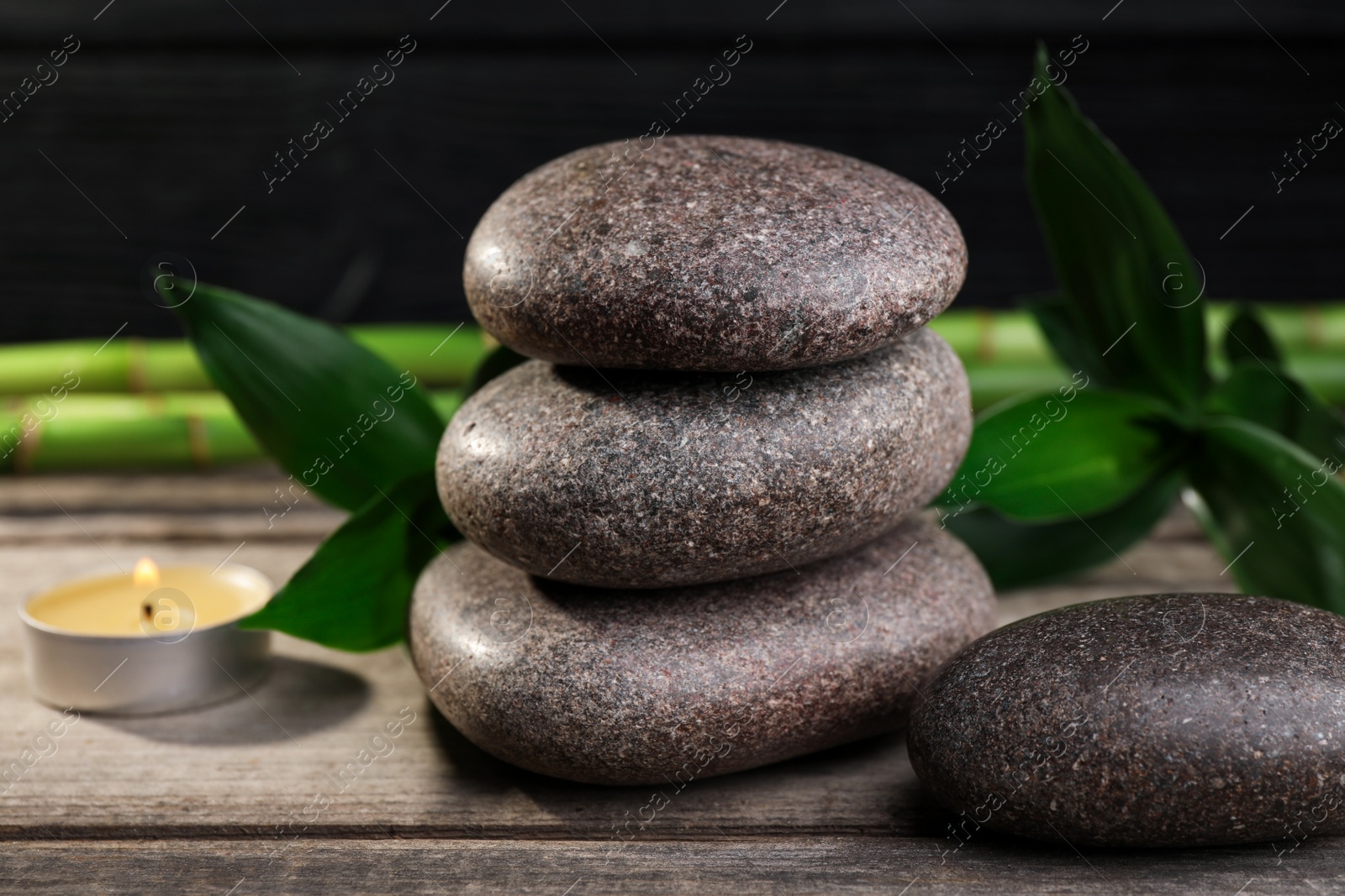 Photo of Spa stones, bamboo and burning candle on wooden table, closeup