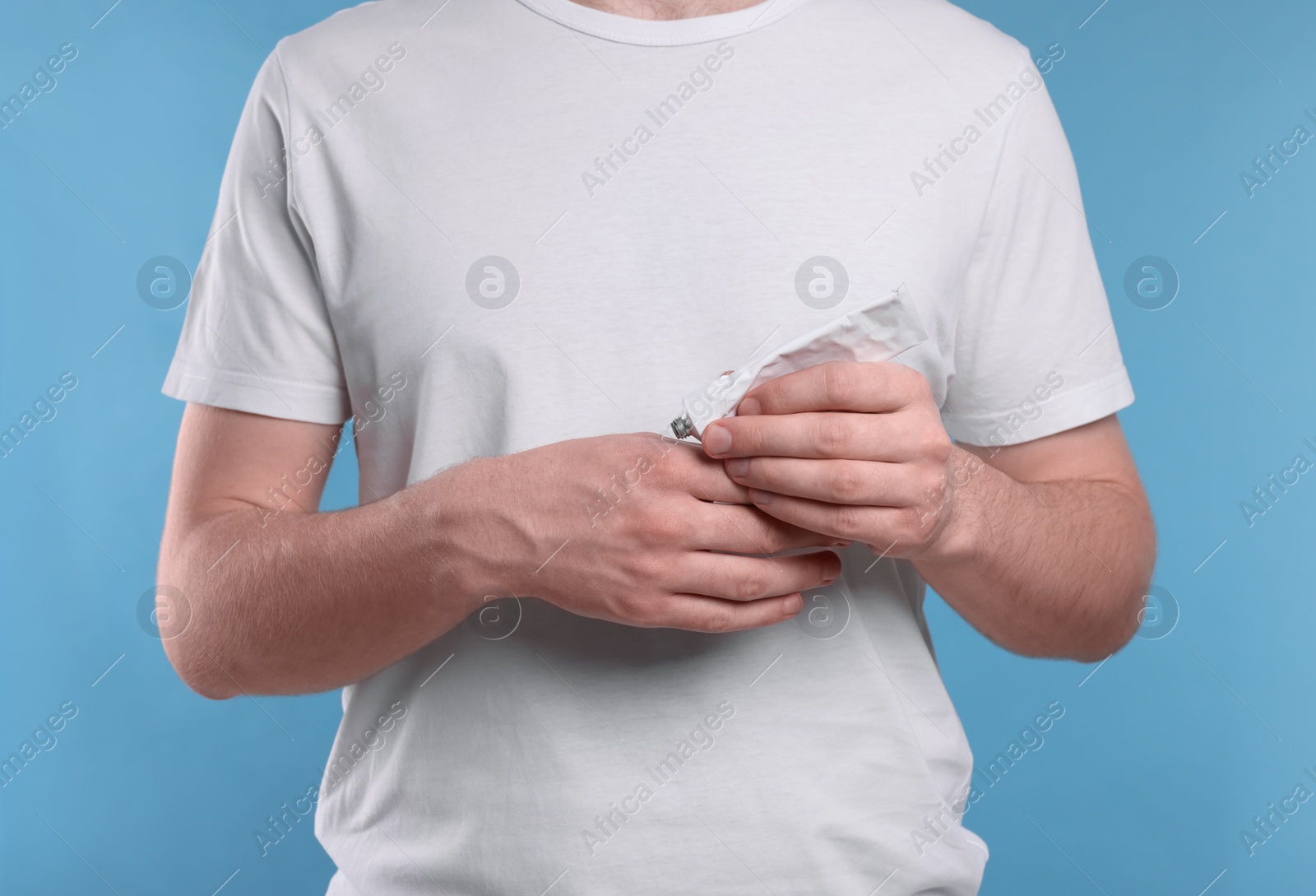 Photo of Man applying ointment from tube onto his hand on light blue background, closeup