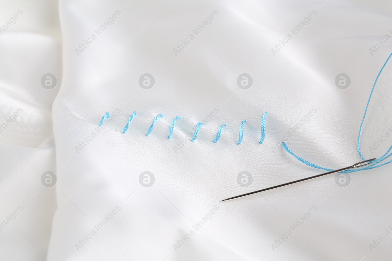 Photo of Sewing needle with thread and stitches on white cloth, top view