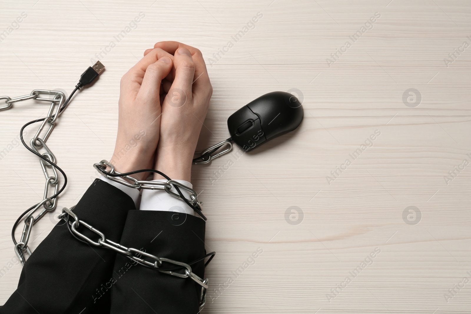 Photo of Man showing hands chained with computer mouse cable at white wooden table, top view. Internet addiction