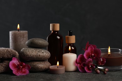 Photo of Beautiful composition with burning candles, spa stones and different care products on dark grey table