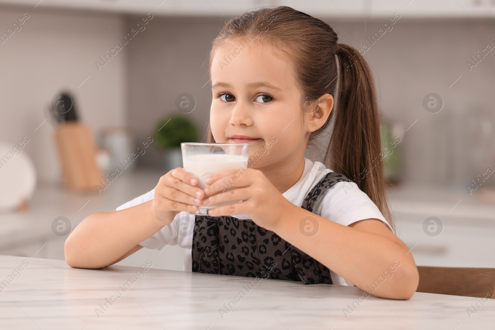 Photo of Cute girl with glass of milk at white table in kitchen