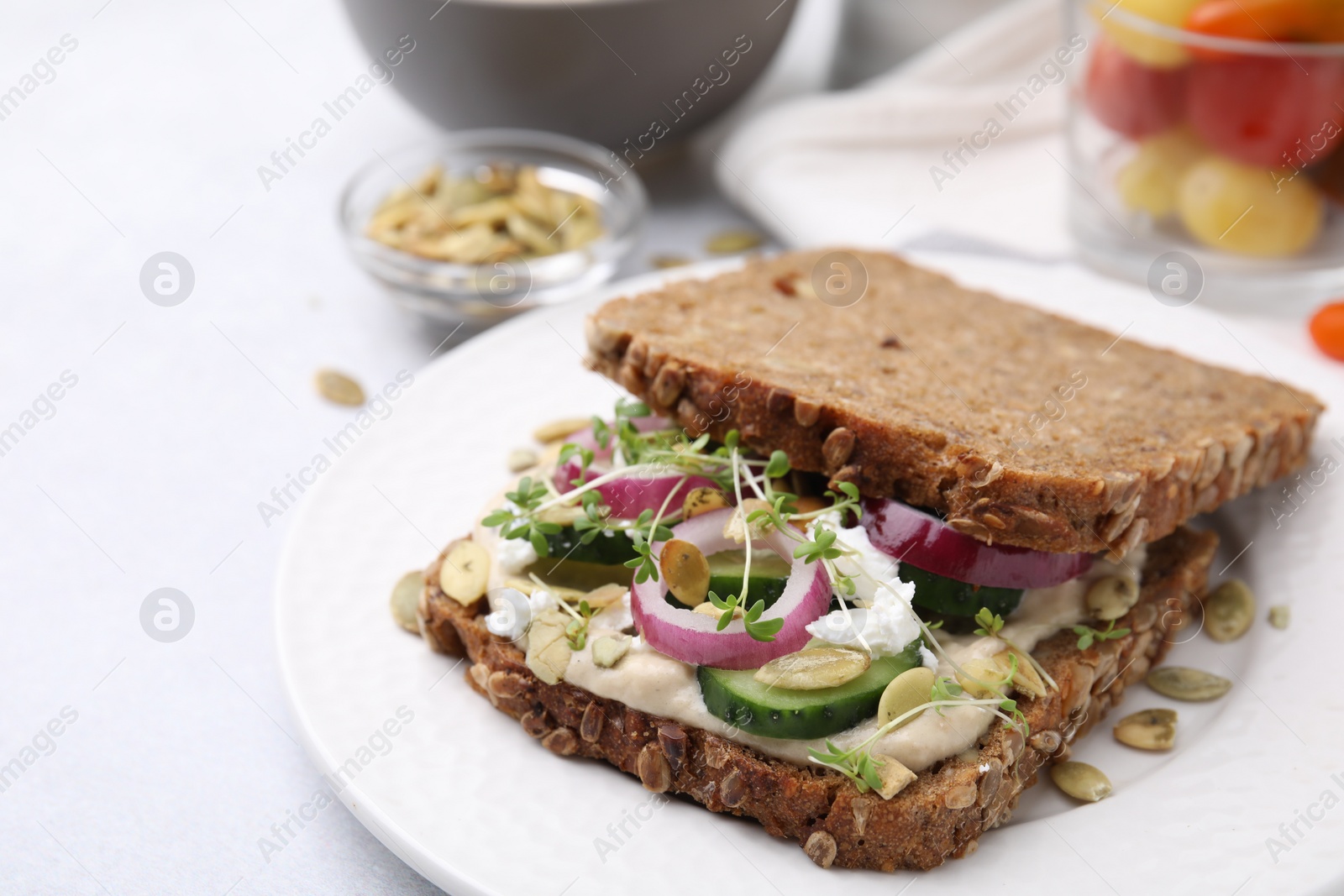 Photo of Tasty vegan sandwich with cucumber, onion, hummus and pumpkin seeds on light grey table, closeup