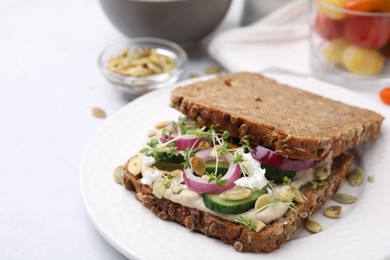 Tasty vegan sandwich with cucumber, onion, hummus and pumpkin seeds on light grey table, closeup