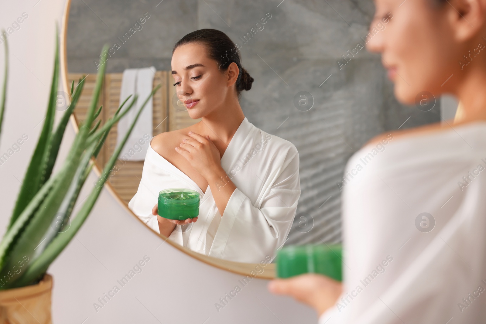 Photo of Young woman applying aloe gel onto her shoulder near mirror in bathroom