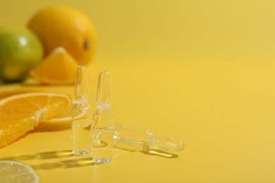 Photo of Skincare ampoules with vitamin C and citrus slices on yellow background, closeup. Space for text