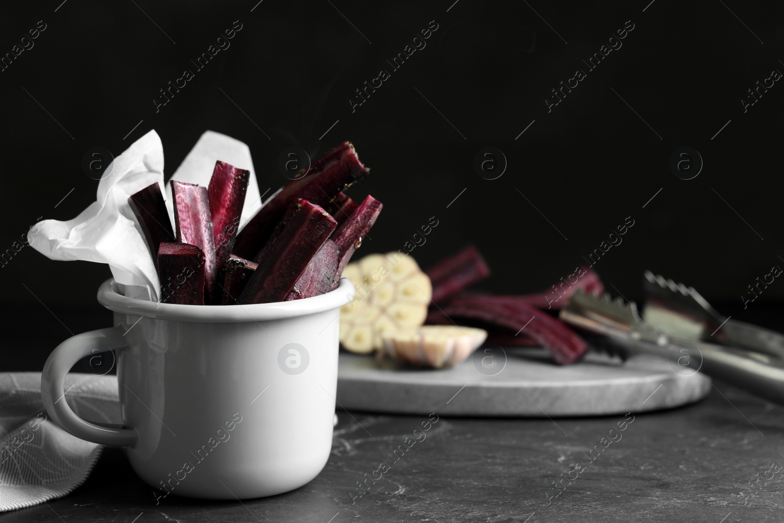 Photo of Tasty cut black carrot in cup on black slate table