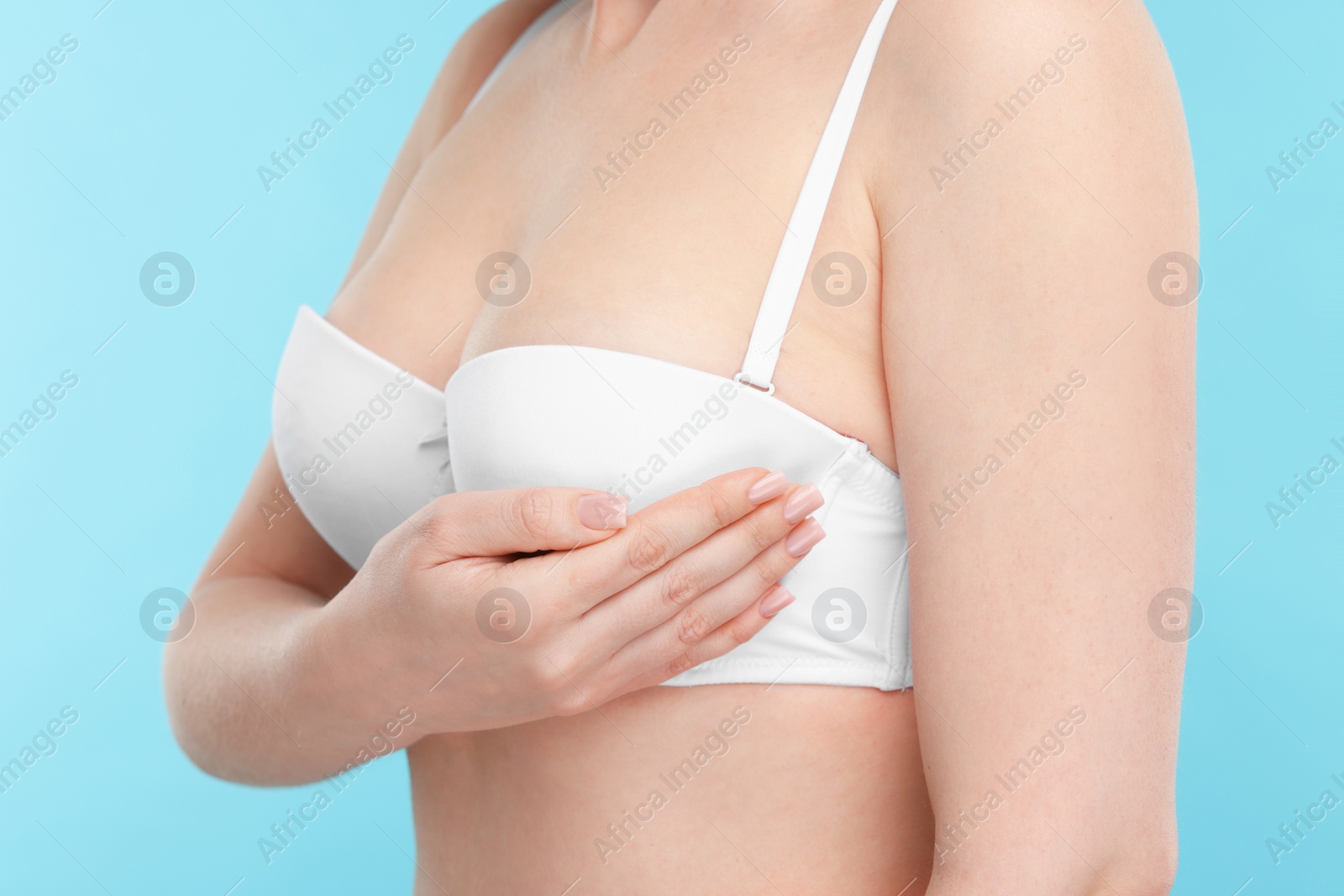 Photo of Mammology. Young woman doing breast self-examination on light blue background, closeup