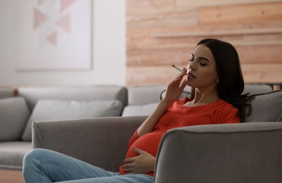 Photo of Young pregnant woman smoking cigarette at home. Space for text