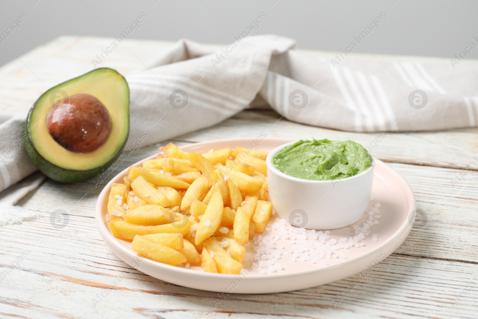 Photo of Plate with french fries, avocado and guacamole dip on white wooden table